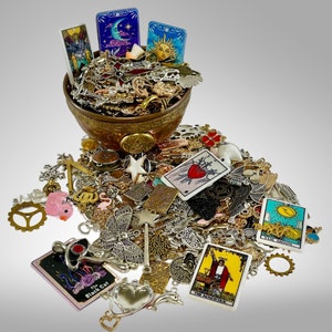 May include: A brown ceramic bowl filled with a variety of silver and gold charms, beads, and pendants. The bowl is surrounded by a collection of tarot cards, including The Magician, The Moon, and The Lovers.