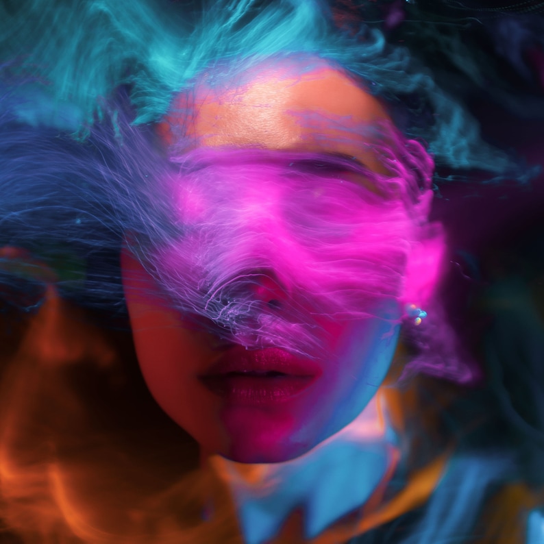 以下が含まれることがあります： 人の顔がピンクとブルーの光の効果で部分的に隠されています。光は顔の周りを流れ、渦巻いているように見えます。その人の唇は鮮やかな赤に塗られています。