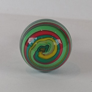 May include: A glass marble with a vibrant swirl pattern in red, green, and yellow. The spherical marble has a glossy surface, reflecting light. The design creates a spiral effect.