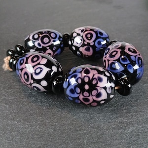 Peut inclure: Un collier de perles en verre noir et blanc avec des tourbillons roses et bleus. Les perles sont de forme ovale et ont une finition brillante.
