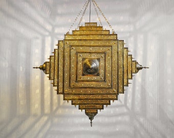 May include: A gold-colored metal chandelier with a square shape and intricate details. The chandelier is made up of multiple layers of squares, each with a decorative pattern. The chandelier is hanging from a chain.