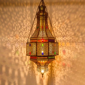 May include: A gold Moroccan lantern with intricate cutouts and colorful glass accents hangs from a chain.