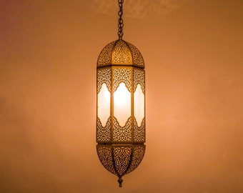 May include: A gold metal hanging lantern with intricate cutouts and a white frosted glass panel. The lantern is lit and casting a warm glow.