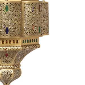 May include: A gold metal lantern with intricate cutouts and colorful glass accents. The lantern has a round top and a pointed bottom.