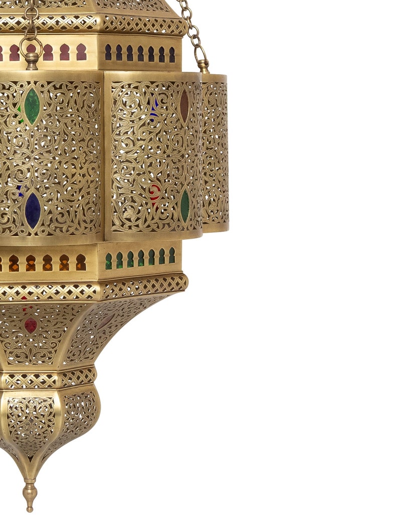 May include: A gold metal lantern with intricate cutouts and colorful glass accents. The lantern has a round top and a pointed bottom.