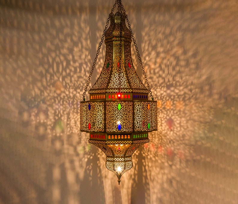 May include: A gold Moroccan lantern with intricate detailing and colorful glass accents hangs from a chain.
