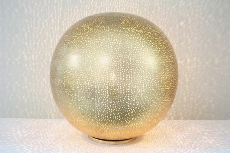 May include: A gold-coloured sphere lamp with a patterned surface. The lamp has a round base and emits a warm glow.