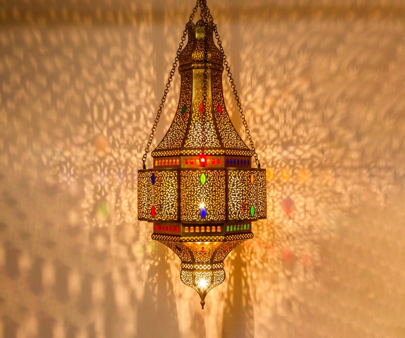 May include: A gold Moroccan lantern with intricate cutouts and colorful glass accents hangs from a chain.