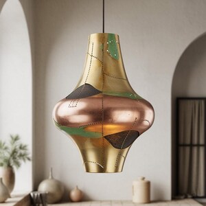 May include: A decorative pendant light fixture with a unique shape. The light has a gold-colored metal finish with copper and green accents. The fixture is suspended from a black cord and is designed to be a focal point in a room.
