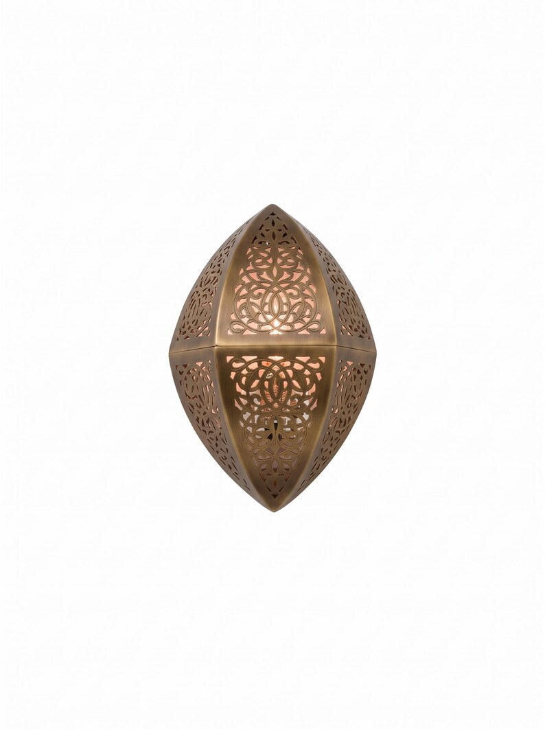 May include: A wall-mounted light fixture with a pointed, almond-shaped metal frame in a muted bronze finish. The surface features intricate, laser-cut filigree patterns that allow warm light to glow from within the hollow, geometric structure.