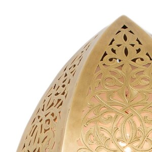 May include: A dome-shaped brass lamp shade featuring intricate laser-cut filigree patterns with swirling floral and vine motifs. The metallic surface has a warm gold tone, and the cutouts reveal a soft, glowing light from within the structure.