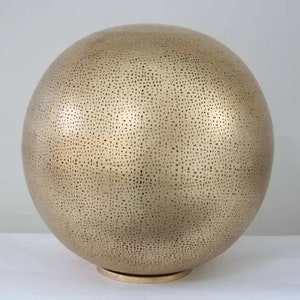May include: A large, gold-coloured, spherical lamp with a textured surface. The lamp has a small, round base.