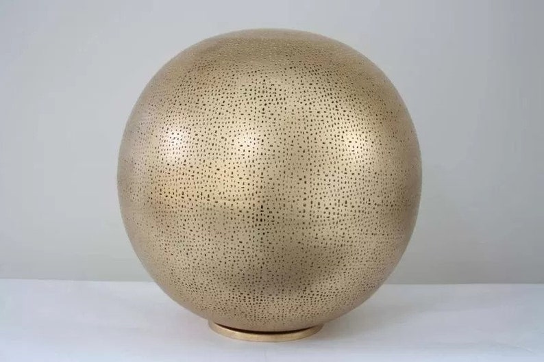 May include: A large, gold-coloured, spherical lamp with a textured surface. The lamp has a small, round base.