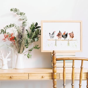 May include: A framed watercolor print featuring five chickens perched on a wooden fence. The chickens are depicted in shades of gray, brown, and black. The artwork is displayed on a light wood desk, alongside a white pitcher with flowers and a decorative deer head.