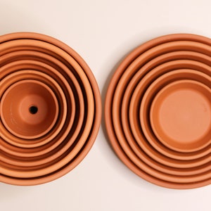 May include: A set of six terracotta plant pots, nested inside each other, with a drainage hole in the smallest pot.