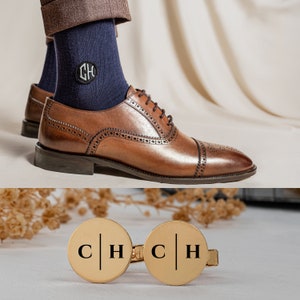 May include: A pair of gold cufflinks with the initials "C H" engraved on each cufflink. The cufflinks are on a white surface.