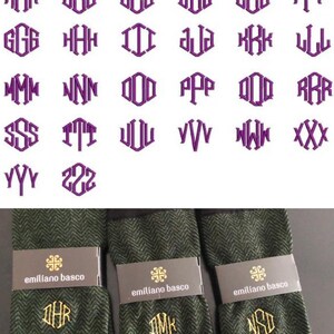 K&ouml;nnte beinhalten: Drei Paar gr&uuml;n-schwarze gemusterte Socken mit goldenen Stickinitialen. Die Socken sind gefaltet und auf einer wei&szlig;en Oberfl&auml;che ausgestellt. Die Initialen sind "DHR", "DMK" und "NSD".