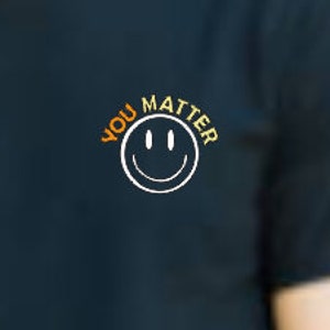 May include: A dark blue t-shirt with the text "YOU MATTER" in orange and yellow lettering, a white smiley face graphic, and a white outline.