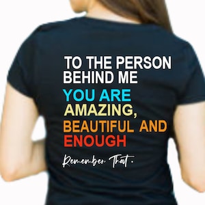 May include: Black t-shirt with the text "To the person behind me, you are amazing, beautiful and enough. Remember that." in colorful text.