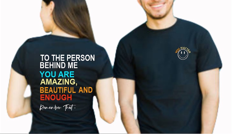 May include: Two black t-shirts with different messages. The front of one shirt says "You Matter" with a smiley face. The back of the other shirt says "To the person behind me, you are amazing, beautiful and enough. Remember that."
