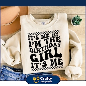 May include: A white sweatshirt with a black graphic that says "It's Me Hi. I'm The Birthday Girl. It's Me." The graphic is surrounded by a black and white checkered border.