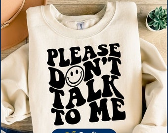 May include: A white sweatshirt with black text that reads "Please Don't Talk To Me" in a retro font. A smiley face is incorporated into the word "Don't".