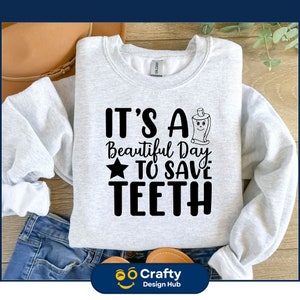 Pu&ograve; includere: Una felpa grigia con il testo "It's a Beautiful Day to Save Teeth" e un'immagine di un tubetto di dentifricio in stile cartone animato.