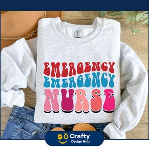 May include: A gray sweatshirt with the text "EMERGENCY NURSE" in a retro rainbow font.