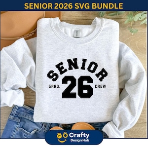May include: A light gray sweatshirt with the text "SENIOR 26" in black block letters. The word "SENIOR" arches above the number "26", with "GRAD." and "CREW" on either side. The sweatshirt is folded on top of blue jeans.