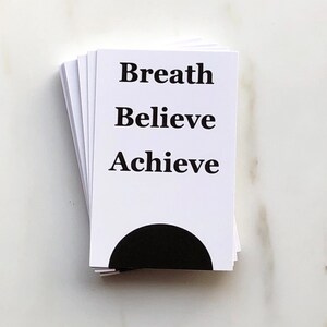 May include: A stack of white cards with black text. The text on the cards reads "Breath", "Believe", and "Achieve".