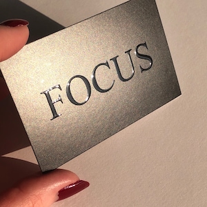 May include: A gray business card with the word "FOCUS" printed in black, raised lettering.