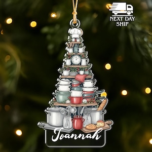 May include: A Christmas tree-shaped ornament featuring a chef's hat at the top and various kitchen items like pots, pans, and utensils. The ornament has a black base with the name "Joannah" in white script.