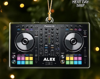 May include: A black Pioneer DJ controller ornament with the name "ALEX" printed on it. The ornament has two circular turntables and colorful buttons. It is hanging from a gold string.