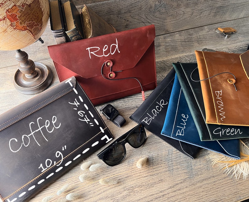 May include: A variety of leather laptop sleeves in different colors, including red, black, blue, green, brown, and coffee. The sleeves are all made of high-quality leather and have a simple, elegant design. Each sleeve has a different color and a handwritten label with the color name.