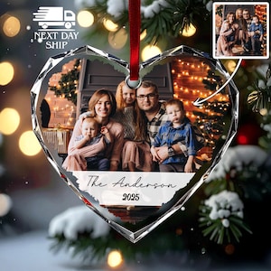 May include: A heart-shaped glass Christmas ornament featuring a printed family photograph of two adults and two children. The ornament has a red ribbon for hanging and includes the text The Anderson 2025 printed in black script and block font.