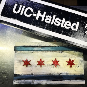 May include: A wooden sign with the text "UIC-Halsted 800W 430S" in white letters on a black background. The sign is sitting on top of a wooden Chicago flag with four red stars on a white background.