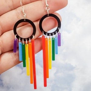 Pu&ograve; includere: Orecchini pendenti arcobaleno con ciondoli circolari neri e strisce acriliche arcobaleno che pendono dal fondo.