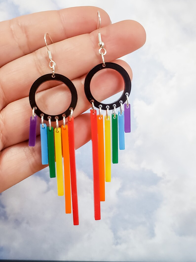 Pu&ograve; includere: Orecchini pendenti arcobaleno con ciondoli circolari neri e strisce acriliche arcobaleno che pendono dal fondo.