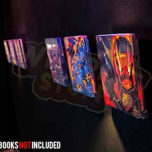 May include: A display of colorful steelbook cases mounted on a dark wall. The cases feature vibrant artwork, including images of characters and scenes. The text "*STEELBOOKS NOT INCLUDED" is visible at the bottom. The cases are arranged in a row.