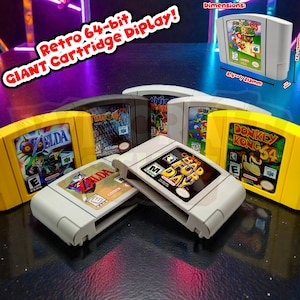Puede incluir: Una colección de cartuchos de videojuegos retro de 64 bits, incluyendo "Super Mario 64", "The Legend of Zelda" y "Donkey Kong 64". Los cartuchos están en carcasas amarillas y grises. La imagen incluye el texto "Retro 64-bit GIANT Cartridge Display!"