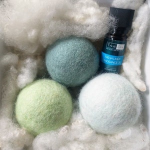 K&ouml;nnte beinhalten: Drei gr&uuml;ne, blaue und wei&szlig;e Woll-Trocknerb&auml;lle mit einer Flasche Fresh Linen Duft&ouml;l. Die Flasche hat einen schwarzen Verschluss und ein wei&szlig;es Etikett mit dem Text "Fresh Linen Fragrance Oil".
