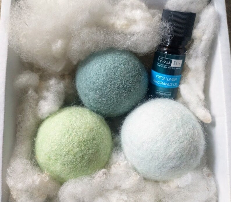 K&ouml;nnte beinhalten: Drei gr&uuml;ne, blaue und wei&szlig;e Woll-Trocknerb&auml;lle mit einer Flasche Fresh Linen Duft&ouml;l. Die Flasche hat einen schwarzen Verschluss und ein wei&szlig;es Etikett mit dem Text "Fresh Linen Fragrance Oil".
