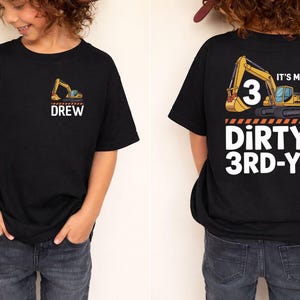 Puede incluir: Camiseta negra con un gráfico de vehículo de construcción y el nombre "DREW" en la parte delantera. La parte trasera de la camiseta dice "IT'S MY 3" con un gráfico de vehículo de construcción y "DIRTY 3RD-Y!" en blanco.
