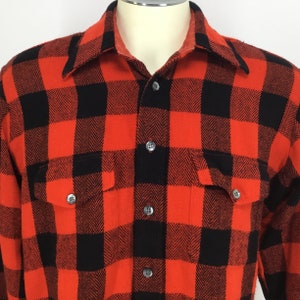Puede incluir: Una camisa de franela a cuadros rojos y negros con cierre de botones y dos bolsillos en el pecho.