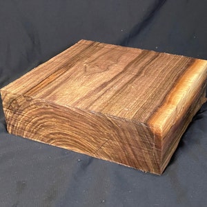 May include: A large block of wood with a rich brown color and a distinctive grain pattern. The wood has a natural, unfinished look.