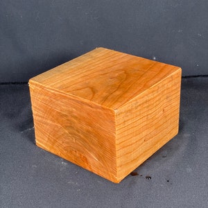 May include: A solid, rectangular wooden block with a natural, light brown color. The wood grain is visible, and the block appears to be freshly cut. The block is likely used for crafts or woodworking projects.