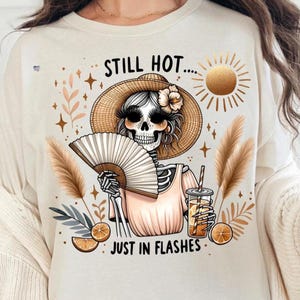 May include: A white t-shirt with a graphic of a skeleton wearing a straw hat and holding a fan. The text "Still Hot... Just in Flashes" is printed on the shirt.