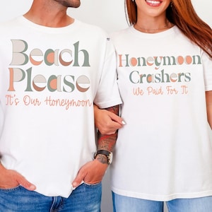 以下が含まれることがあります： お揃いのテキストが入った白いTシャツ2枚。1枚はレトロなフォントで「Beach Please It's Our Honeymoon」と書かれています。もう1枚は「Honeymoon Crashers We Paid For It」と書かれています。どちらのシャツもゆったりとしたフィット感で、カップルに最適です。