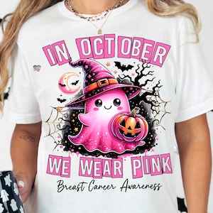 Peut inclure: T-shirt blanc avec un motif rose d'un fant&ocirc;me portant un chapeau de sorci&egrave;re et tenant une citrouille. Le texte "In October We Wear Pink" et "Breast Cancer Awareness" est imprim&eacute; en rose.