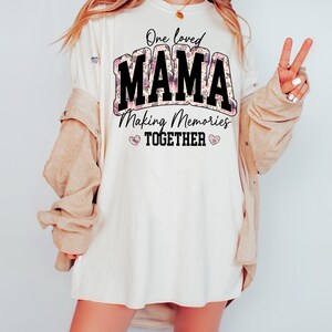 May include: White t-shirt with a floral design and the text "One loved MAMA Making Memories TOGETHER" in black.
